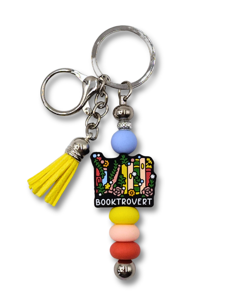 kolorowy i radosny breloczek dla fanów książek i czytania z napisem: Booktrovert, książkami i kwiatkami.