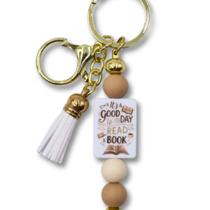 stylowy breloczek w odcieniach beżu, bieli i złota z motywem "It's a good day to read a book" idealny prezent dla miłośniczek czytania