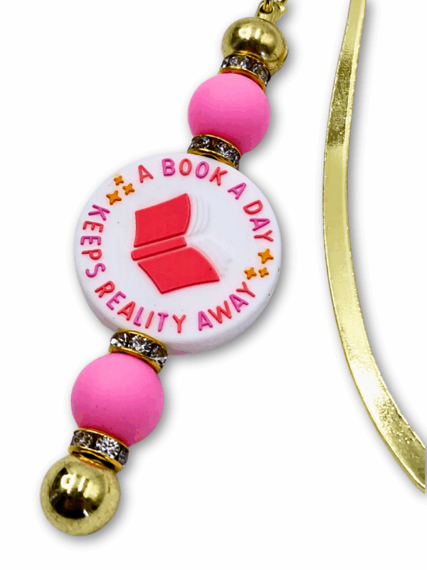 zakładka z napisem book a day keep reality away jest różowa a metal w kolorze złota