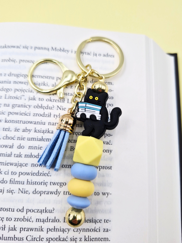 złoty breloczek pastelowy z kotem i książkami dla miłośniczki kotów i książek zabawny gadżet i prezent dla książkary kociary